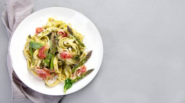 Gri arka planda kuşkonmaz ve jambonlu makarna. Geleneksel İtalyan yemeği konsepti. Üst görünüm, düz görünüm, kopyalama alanı