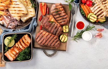 Grilled fish, seafood and meat assortment on light background. Homemade food concept. Top view, flat lay, copy space clipart