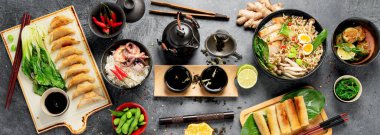 Karanlık arka planda çeşitli malzemeli Asya yemekleri. Panorama.