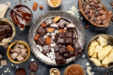 Çikolata, ezilmiş çikolata parçaları, kakao çekirdekleri, kakao yağı, fındık, koyu arkaplan manzarası..