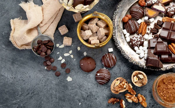 Çikolata, ezilmiş çikolata parçaları, kakao çekirdekleri, kakao yağı, fındık, koyu arkaplan manzarası..