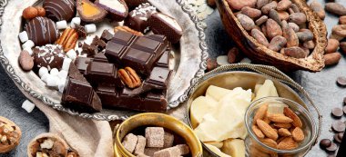 Çikolata, ezilmiş çikolata parçaları, kakao çekirdekleri, kakao yağı, fındık, koyu arkaplan manzarası, panorama..