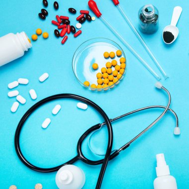 Çeşitli tıbbi ekipmanlar, ampuller, pipet, ilaçlar, haplar, kapsüller, mavi arka planda sprey. Üst görünüm.