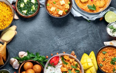 Hint mutfağı tabakları. Köri, tereyağlı tavuk, pilav, mercimek, paneer, samosa, baharatlar. Koyu arkaplanlı Hint yemeği tabakları. Kopyalama alanı olan üst görünüm.
