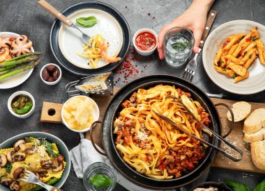 İtalyan yemekleri, makarna soslu makarna, mantı, tavuk soslu makarna, parmesan peyniri ve koyu arkaplanda su. Üst görünüm.