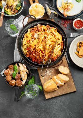 İtalyan yemekleri, makarna soslu makarna, mantı, tavuk soslu makarna, parmesan peyniri ve koyu arkaplanda su. Üst görünüm.