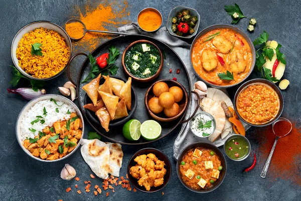 Dishes of indian cuisine. Curry, butter chicken, rice, lentils, paneer, samosa, spices. Bowls and plates with indian foodon dark on dark background.