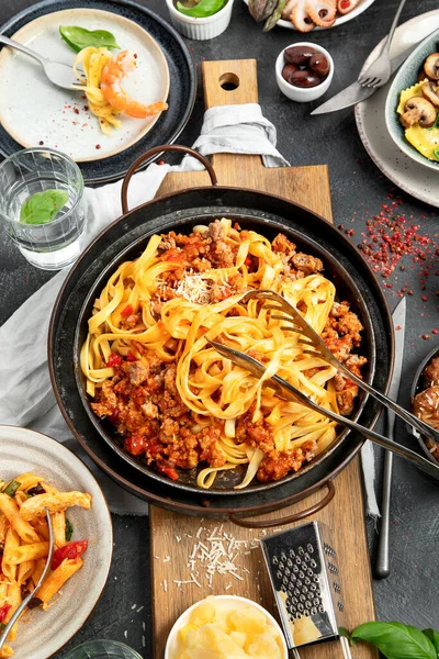 İtalyan yemekleri, makarna soslu makarna, mantı, tavuk soslu makarna, parmesan peyniri ve koyu arkaplanda su. Üst görünüm.