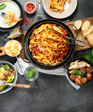 İtalyan yemekleri, makarna soslu makarna, mantı, tavuk soslu makarna, parmesan peyniri ve koyu arkaplanda su. Üst görünüm.