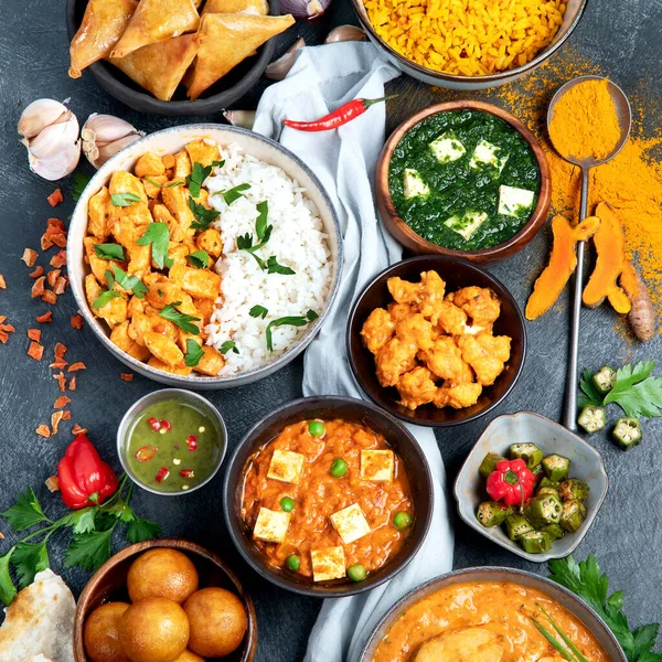 Dishes of indian cuisine. Curry, butter chicken, rice, lentils, paneer, samosa, spices. Bowls and plates with indian foodon dark on dark background. Top view.