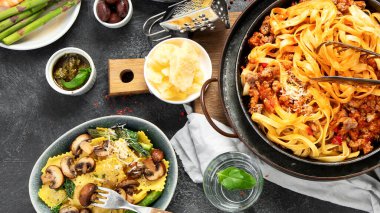 İtalyan yemekleri, makarna soslu makarna, mantı, tavuk soslu makarna, parmesan peyniri ve koyu arkaplanda su. Üst görünüm.