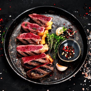 Biberli ızgara biftek, otlar ve siyah arka planda bir tabakta tuz. Üst görünüm