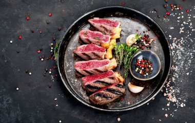 Grilled beef steaks with pepper, herbs and salt on a plate on a dark background. Top view.