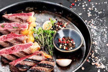 Biberli ızgara biftek, otlar ve siyah arka planda bir tabakta tuz. Üst görünüm.