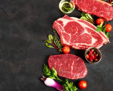 Koyu arka planda baharat ve çatal bıçaklarla ızgara yapmak için çiğ et bifteği çeşitliliği..