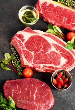 Koyu arka planda baharat ve çatal bıçaklarla ızgara yapmak için çiğ et bifteği çeşitliliği..