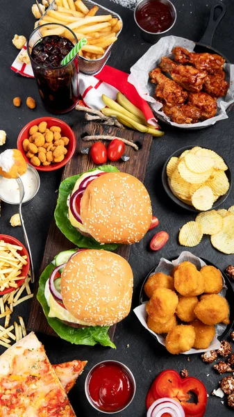 Fast food and unhealthy eating concept - close up of fast food snacks and cola drink on a dark background, top view.
