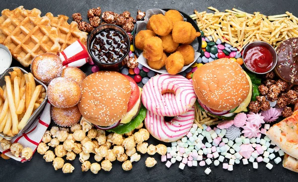 Unhealthy products. food bad for figure, skin, heart and teeth. Assortment of fast carbohydrates food with fries and cola on a dark background. Top view.