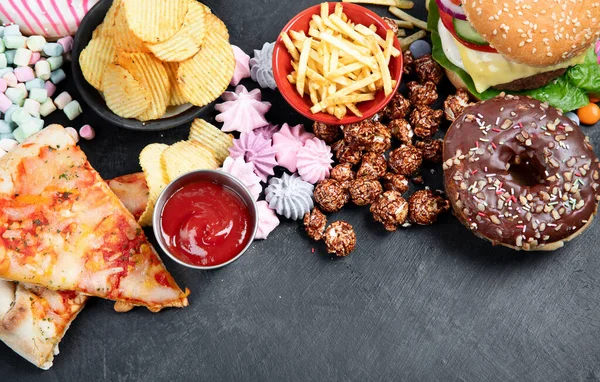 Unhealthy products. food bad for figure, skin, heart and teeth. Assortment of fast carbohydrates food with fries and cola on a dark background. Top view.