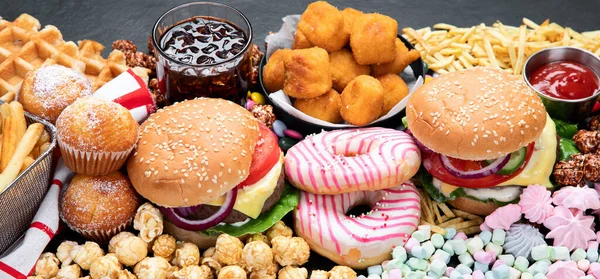 Unhealthy products. food bad for figure, skin, heart and teeth. Assortment of fast carbohydrates food with fries and cola on a dark background. Top view. Panorama.