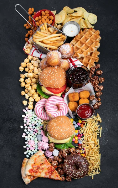 Unhealthy products. food bad for figure, skin, heart and teeth. Assortment of fast carbohydrates food with fries and cola on a dark background. Top view.
