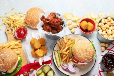 Various of american food, French fries, hamburgers, nuggets, hotdog, chips, popcorn, sauces on a white background, top view.