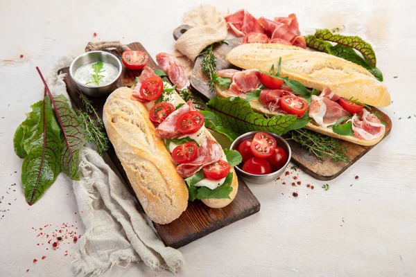 Two baguette sandwiches with salami, mozzarella cheese, lettuce, tomatoes and ham on a cutting boards. Long subway sandwiches on a white background. Top view.