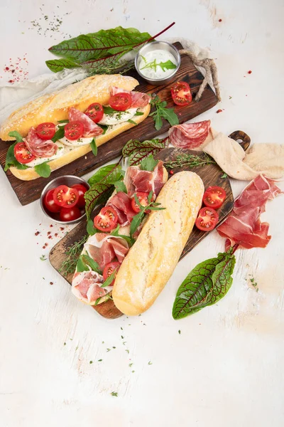 Two baguette sandwiches with salami, mozzarella cheese, lettuce, tomatoes and ham on a cutting boards. Long subway sandwiches on a white background. Top view.