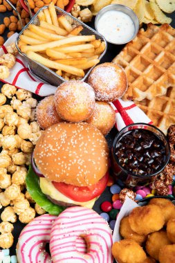Sağlıksız ürünler. Yemek vücut, deri, kalp ve dişler için kötüdür. Fast karbonhidrat karışımı. Arka planda patates kızartması ve kola var. Üst görünüm.