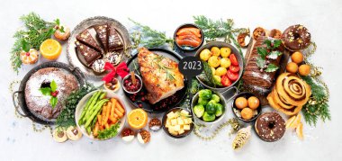 Delicious Christmas themed dinner table with roasted meat, potato, appetizers and desserts. Holiday concept. Top view on a grey background. Holiday concept.