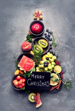 Karanlık arka planda meyvelerden yapılmış Noel ağacı. Yeni yıl tatili konsepti. Üst görünüm, düz görünüm, kopyalama alanı