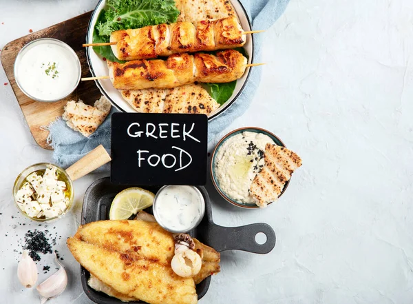 Greek food background. Meze, gyros, souvlaki, fish, pita, greek salad, tzatziki, assortment of feta, olives and meatballs. Traditional different greek dishes set. on a grey background. Top view with copy space.