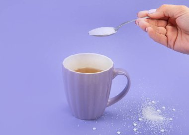 Bir fincan çaya düşen şekerli el. Menekşe arkaplanda suni şeker, üst görünüm.