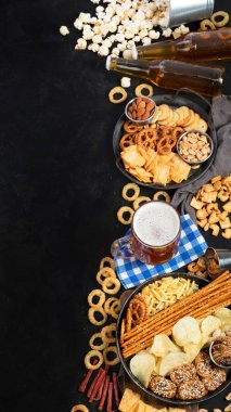 Koyu arka planda çeşitli bira ve tuzlu atıştırmalıklar. Parti yemeği konsepti. Üst görünüm, alanı kopyala