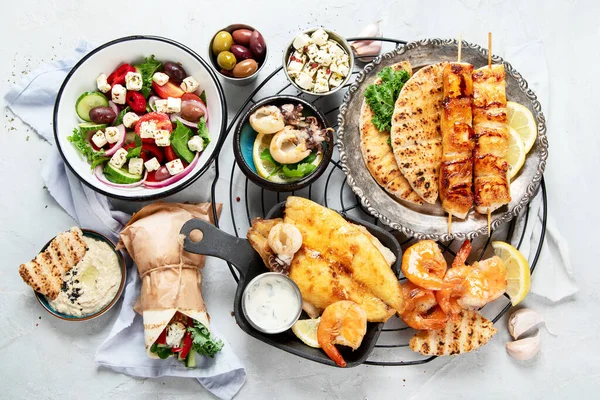 Greek food background. Meze, gyros, souvlaki, fish, pita, greek salad, tzatziki, assortment of feta, olives and meatballs. Traditional different greek dishes set. on a grey background. Top view.