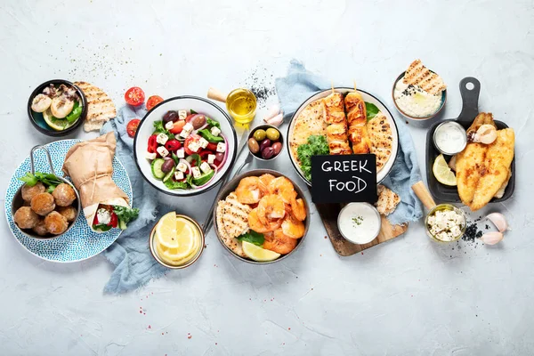 Greek food background. Meze, gyros, souvlaki, fish, pita, greek salad, tzatziki, assortment of feta, olives and meatballs. Traditional different greek dishes set. on a grey background. Top view.