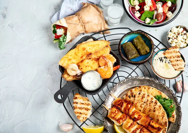 Greek food background. Meze, gyros, souvlaki, fish, pita, greek salad, tzatziki, assortment of feta, olives and meatballs. Traditional different greek dishes set. on a grey background. Top view with copy space.