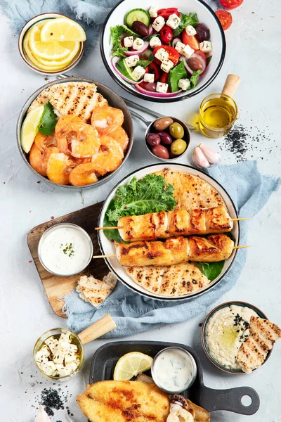 Greek food background. Meze, gyros, souvlaki, fish, pita, greek salad, tzatziki, assortment of feta, olives and meatballs. Traditional different greek dishes set. on a grey background. Top view.