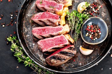 Biberli ızgara biftek, otlar ve siyah arka planda bir tabakta tuz. Üst görünüm.