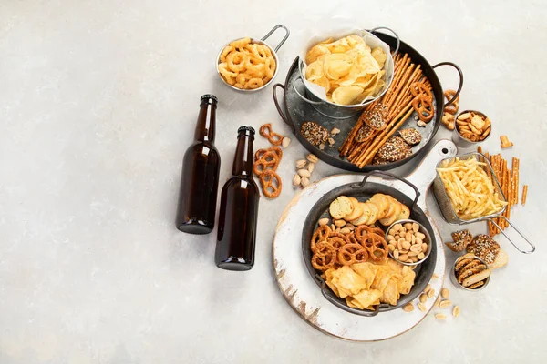 Assortment of beer and salty snacks on light background. Party food concept. Top view, copy space