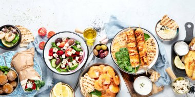Yunan yemek geçmişi. Meze, gyros, souvlaki, balık, pide, Yunan salatası, tzatziki, çeşit çeşit feta, zeytin ve köfte. Geleneksel Yunan yemekleri seti. Gri bir arka planda. Üst görünüm.