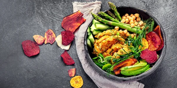 Vegan buddha bowl. Bowl with  vegetables, Zucchini fritters and vegetables chips. Dark background. Healthy eating concept. Top view, copy space