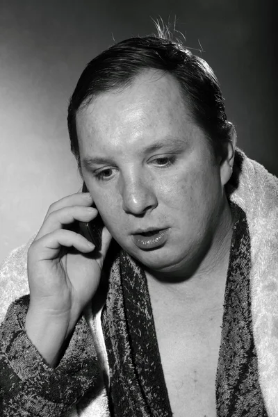 Young man in a bathrobe talking on a cell phone — Stock Photo, Image