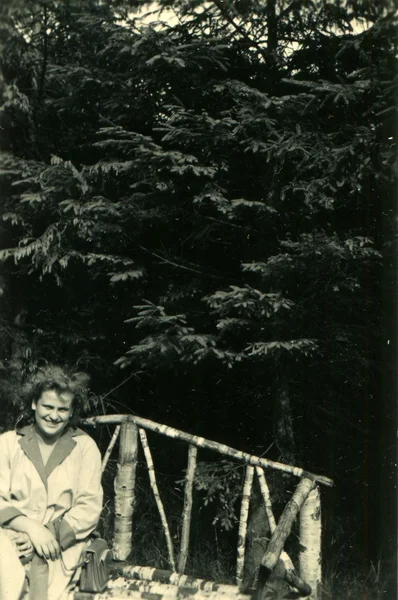 Mujer joven en el asiento del abrigo en el banco en el bosque — Foto de Stock