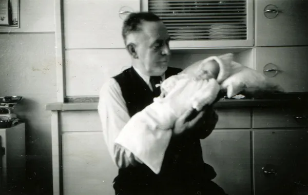 Man in a waistcoat, white shirt and tie holding a baby in diapers