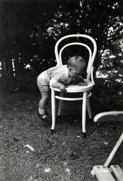 Little boy climbs on white bentwood chair in the garden — Stock Photo, Image