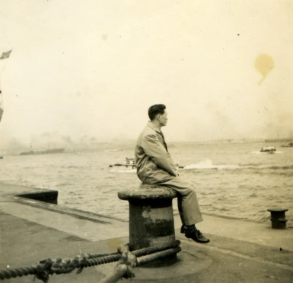 Man sitter på en pollare i dock titta på havet — Stockfoto