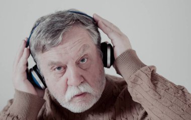 Beyaz arka planda kulaklık takmış yaşlı beyaz bir adamın portresi.