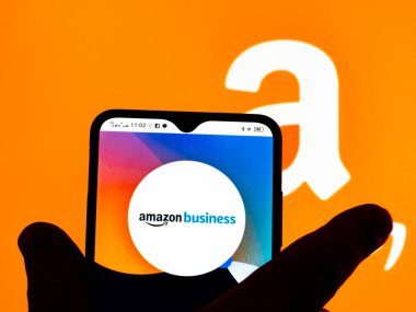 Kiev, Ukraine - January 12, 2022: In this photo illustration, the Amazon Business logo is seen displayed on a smartphone screen and Amazon logo in the background. 