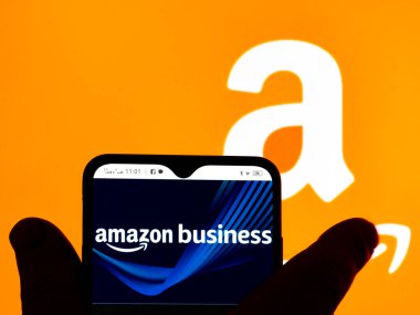 Kiev, Ukraine - January 12, 2022: In this photo illustration, the Amazon Business logo is seen displayed on a smartphone screen and Amazon logo in the background. 